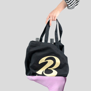Eine schwarze Tasche mit dem Bott1e-Logo steht auf einem Fuß. Eine Hand greift nach der Tasche.