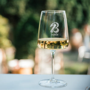 Ein Glas mit Weißwein und einem Bott1e-Logo steht auf einem Tisch.