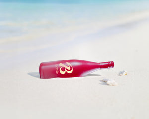 Eine rote Weinflasche mit Bott1e-Logo liegt am Strand.
