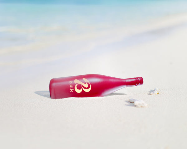 Eine rote Weinflasche mit Bott1e-Logo liegt am Strand.