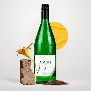 Eine Weinflasche Josef Ambs, Grauer Burgunder, Trocken, 1 Liter-Flasche, links daneben liegt ein Stein mit einer gelben Blume.